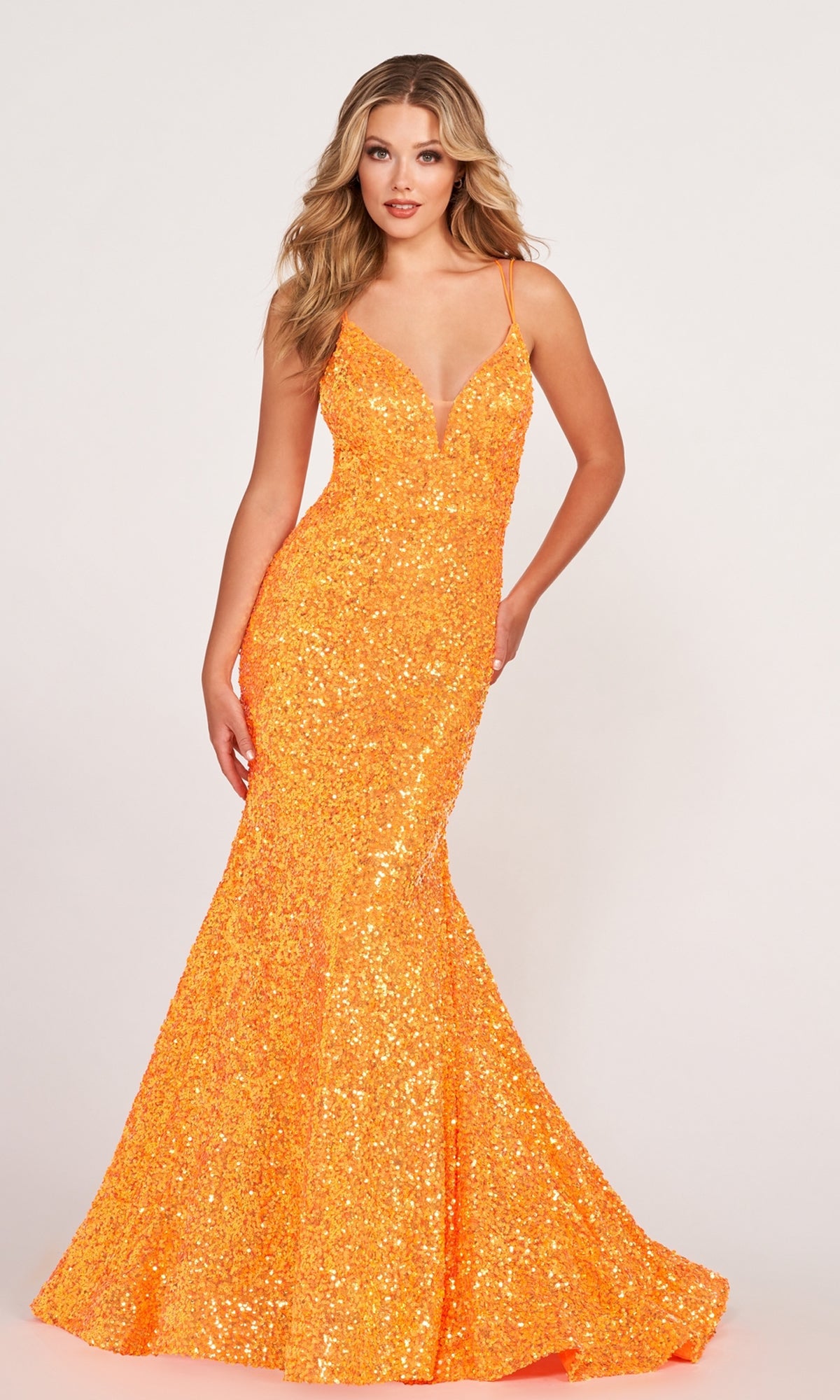A woman models the Ellie Wilde Long Stretch-Sequin Prom Dress—a bright orange, fitted, floor-length gown with thin straps, strappy back, and a slight mermaid flare—against a plain light background.